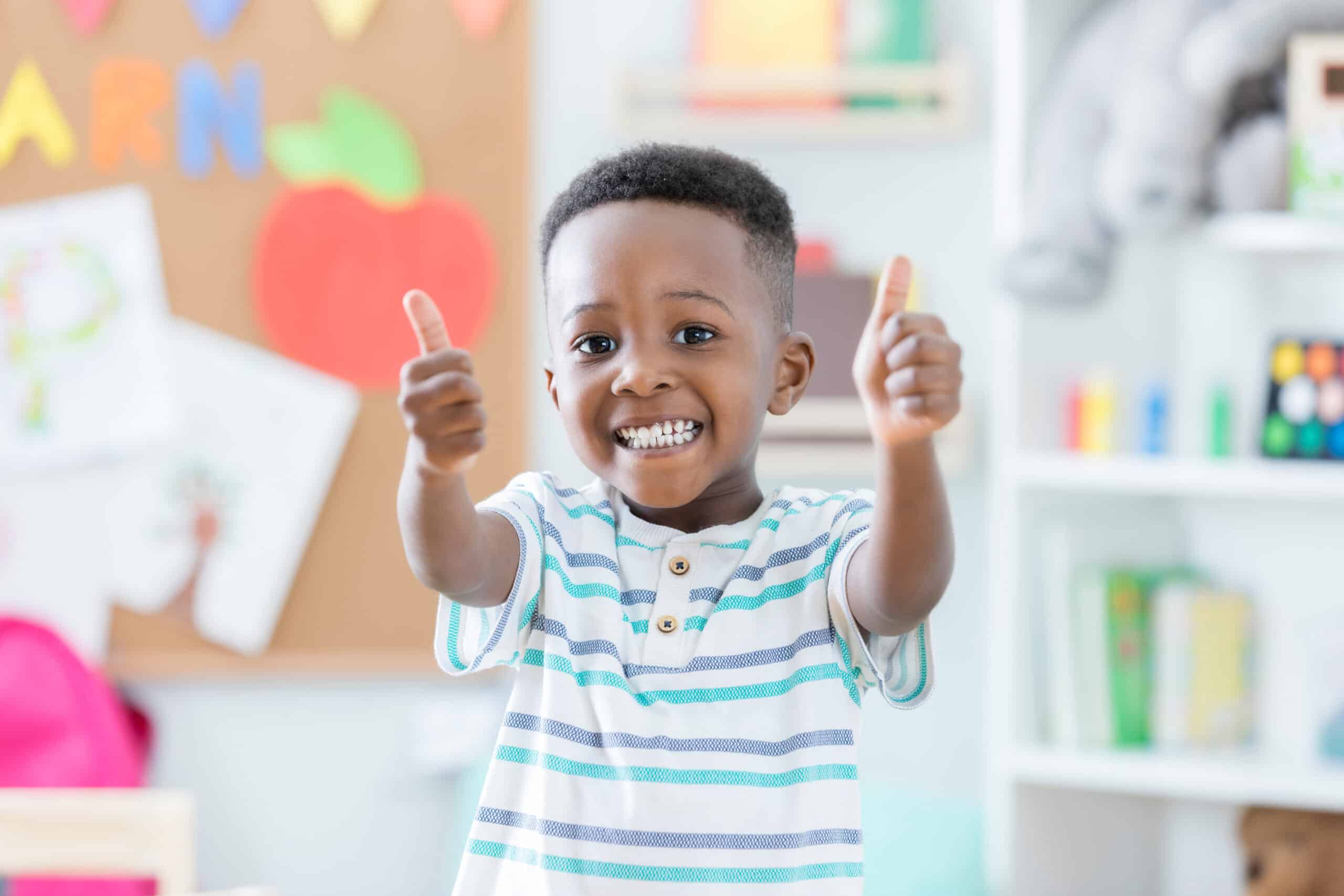 A boy in a classroom giving a double thumbs up.