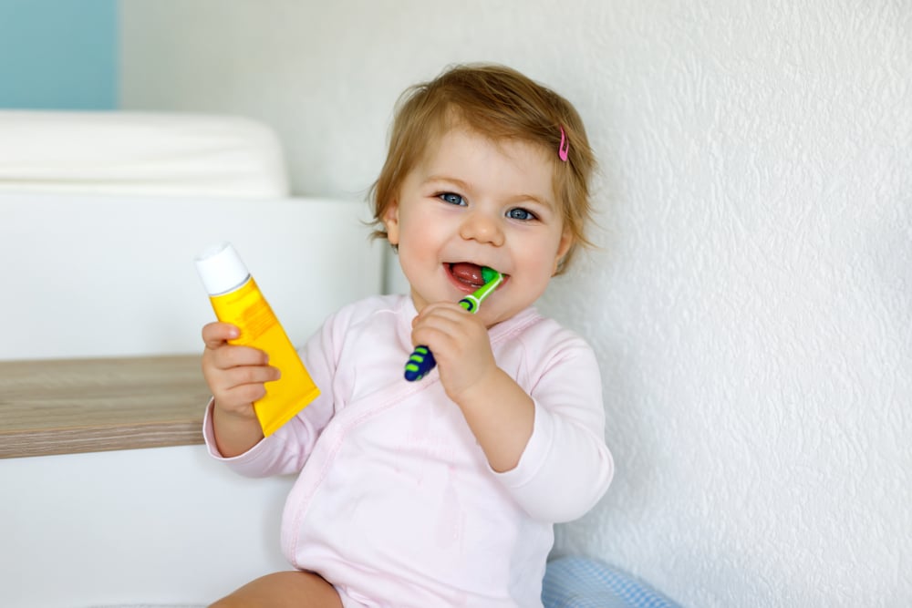 a little girl brushing her teeth and holding a bottle of toothpaste